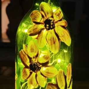 A hand-painted wine bottle featuring delicate flowers illuminated by soft light, creating a warm and inviting ambiance.